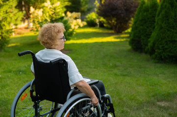 Happy elderly woman sitting in a wheelchair on a walk outdoors. 