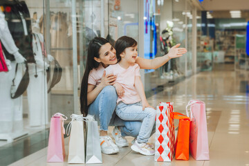 young mother and daughter holding shopping bags, shopping in the mall. Family shopping.