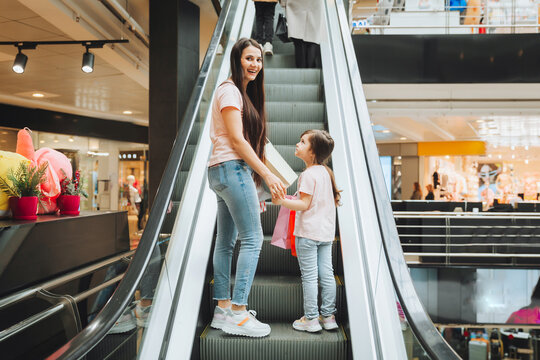 Mother And Little Girl On The Escalator In The Mall.Mother And Daughter In The Mall. A Young Mother And Her Little Child Are Shopping Together.