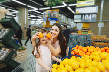 Family in the supermarket. young mother and her little daughter are smiling and buying food. Healthy food concept. mom and daughter buy vegetables and fruits in the supermarket