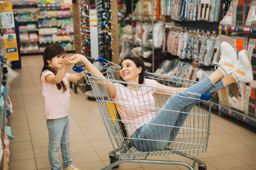 In the supermarket: a daughter pushes a cart with a woman sitting in it, a happy family rushes...