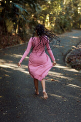 young woman with braids running barefoot along a path in the forest in a pink dress