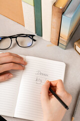 a hand holding black pen ready to write in open notebook. The books on the background.