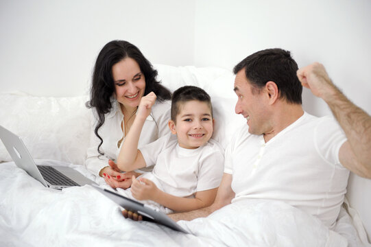 husband wife in bed with little son looking at tablet cartoon interesting game pictures laughing talking communication real people at home love life happy family with tablet pc in bed at home