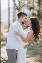 Stylish groom in white shirt and cute brunette bride in white dress in forest near wedding wooden arch. Wedding portrait of newlyweds.