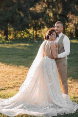 Wedding photo. The bride and groom are standing in a beautiful forest and beautiful light, hugging. Couple in love. Stylish groom. Portrait