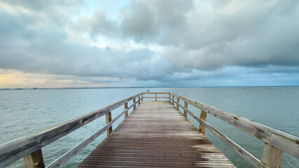 Empty wooden pier with dramatic sky and calm water