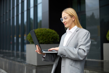 Successful smiling blonde  businesswoman using laptop computer, typing on keyboard working online...