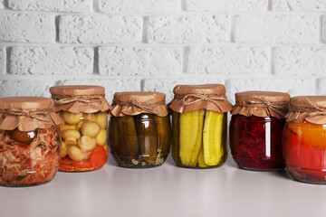 Many glass jars with different preserved vegetables and mushrooms on light grey table