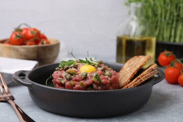Tasty beef steak tartare served with yolk, capers and bread on light grey table