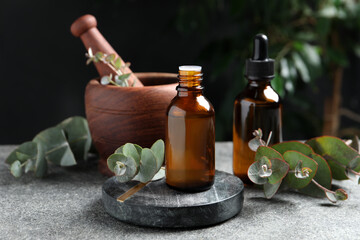 Bottles of eucalyptus essential oil, leaves and mortar on light grey table