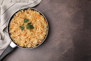 Frying pan with sauerkraut on brown table, top view. Space for text