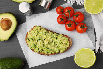Delicious sandwich with guacamole, tomatoes and limes on gray wooden table, flat lay