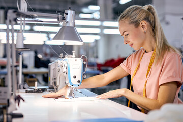 nice caucaian blonde textile factory worker on production line using modern sewing machine, at...