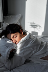 young black-haired man sleeping deeply in the bedroom, embracing pillow, has dread. close up side view portrait
