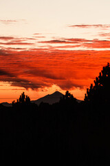 Obraz premium Sunrise with the sun's rays leaving the horizon, reflecting in the clouds and in the background a volcano.