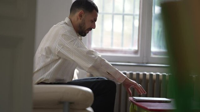 One candid young man sitting on couch at home opening laptop computer
