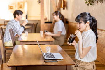 カフェでコーヒーを飲みながらリモートワークするアジア人女性
