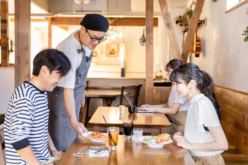 カフェ・飲食店で食べ物を運ぶホールスタッフ・店員と客
