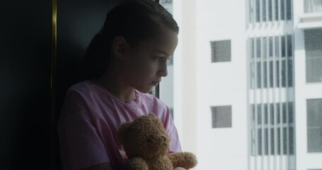 Cute little girl portrait child is sad in her room with a toy in her hands, child in depression in the room with a toy bear in his hands. Sad family. Fear of child in dark. Family violence concept. 4K - Powered by Adobe