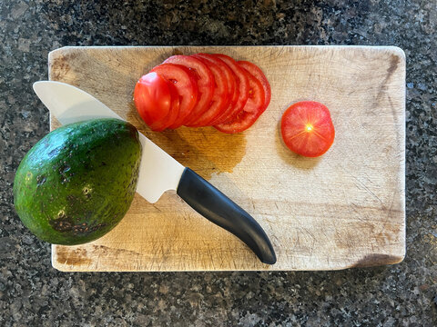 Avocado with tomato on a wooden cutting board with a ceramic knife
