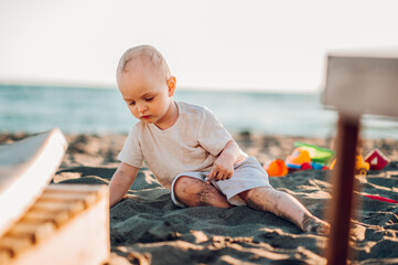 Little cute boy sitting on a tropical beach playing in the sand with toys.
