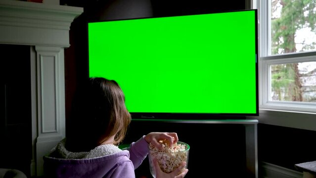 Woman Watching Green Chroma Key Screen TV Relaxing. Girl in Cozy Room Watching Sports Match, News, Sitcom TV Show or a Movie on Green Screen eating popcorn and Change TV channels
