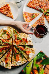 Traditional Italian pizza, vegetables, ingredients on a light background.Top view. a piece of pizza in the hand.Festive table. company of friends