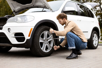 Naklejka na ściany i meble Pensive man changes tire on SUV outdoors. Car repair concept