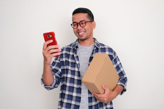 Adult Asian man bring a package box and looking to his handphone with happy expression