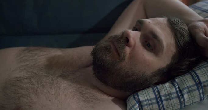 Sad depressed beard man lying on the couch. Unkept, dreamy, pensive look. Thinking about something. Close up. Sadness, depression concept