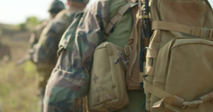 young fully equiped men marching walking along field road In Autumn Day. Group of Soldiers Marching In Forest. back view slow motion
