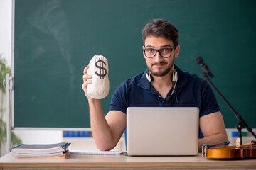 Young male music teacher holding moneybag in the classroom