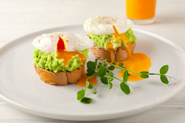 European breakfast. Toasted bread with avocado, poached egg and fruit juice on a white wooden table. healthy diet food