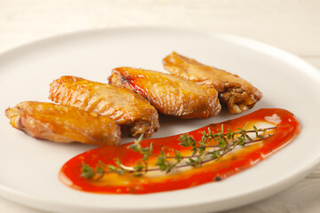 Grilled spicy chicken wings with ketchup on a plate on a white background.
