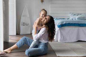 Cheerful caring mom holding adorable little kid in arms, hugging girl with check touch, smiling,...