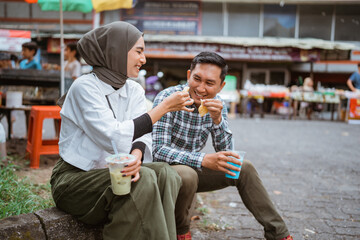 beautiful muslim couple sitting on a road side and enjoy the food they bought from street vendor during ramadan