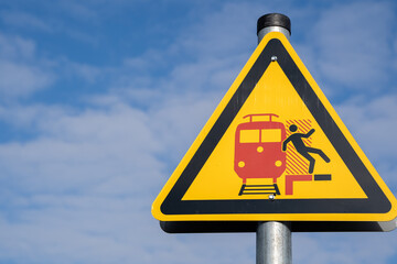 Yellow triangular warning sign on a platform in germany for people to pay attention to passing...