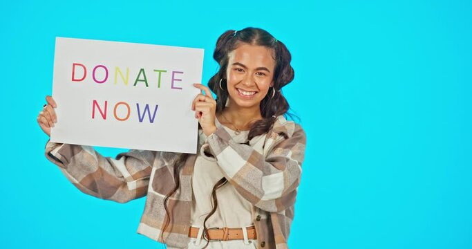Face, smile and woman with donate now sign, poster and support against a blue studio background. Portrait, female volunteer and happy person with banner, community solidarity and helpful with charity