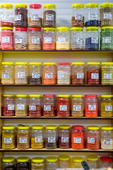 a large selection of different spices on the store shelf. Text in Russian: cumin, coriander, cinnamon, pepper, Zira, mustard, cloves, paprika, garlic.