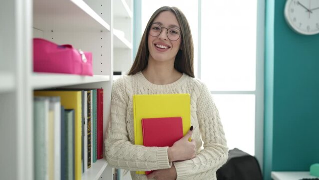 Young beautiful hispanic woman standing holding books at library university