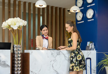 Female receptionist giving hotel information to woman traveller at  check in counter.