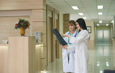 Two females doctor examining and discussing patient's x-ray film in corridor of hospital..