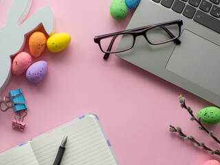 Easter work concept. Flat lay. Business work desk with devices and happy easter holiday multicolored eggs on pink background. Spring decoration workplace with gadgets. Work day on Easter holidays.