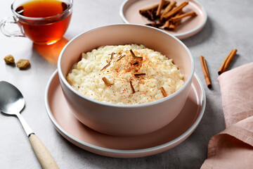 Fresh prepared rice pudding garnished with cinnamon flakes and served with cup of tea. Healthy breakfast for every day. Gray background.
