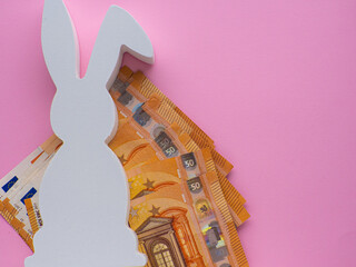 White Easter bunny with Euro banknotes on pink background. Easter and saving, spending money concept. Expensive celebration and shopping of the Easter holidays. Saving money for gifts