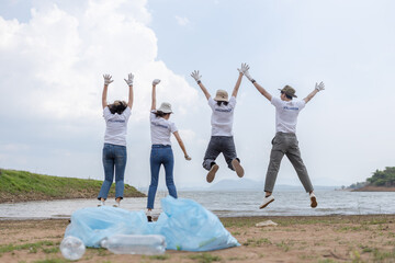 Group of volunteers cheerful success jumping together and arms raised with rubbish bags foreground. clean up garbage in tourist attractions. Conservation and care cleanliness in nature.