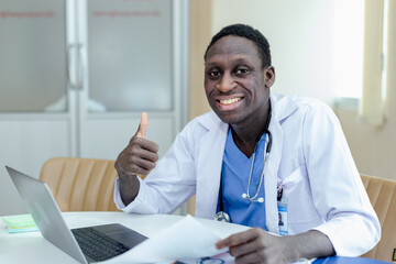 Happy African American man doctor thumbs up sitting at clinic office desk raising hand to greet patient online via laptop communication. health treatment concept. Tele health medicine.