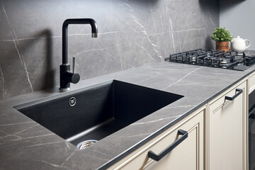 Kitchen sink area with black square matte sink tap in contemporary style. Matte black and stoneware kitchen design. Black ceramic sink with gas hob and oven in background. - obrazy, fototapety, plakaty
