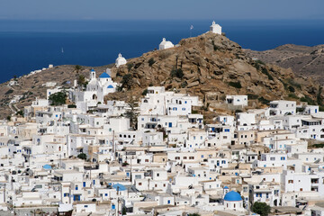 Panoramic view of a church, smaller chapels and the Greek flag on the top of a hill overlooking the Aegean Sea in  Ios in Greece, also known as Chora